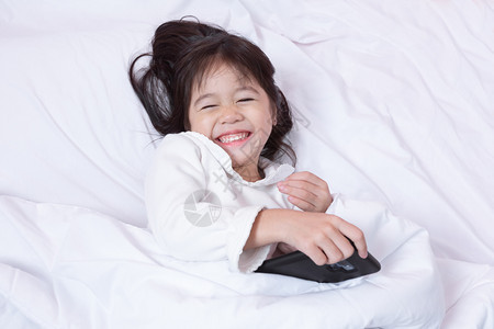 卧室亚洲小孩玩智能手机得开心早上躺在床坐软枕头笑起来感觉很快乐的喜悦青少年幸福图片
