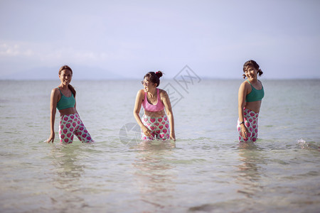 海滨蓝色的身体穿瑜伽西装的三名亚裔女站在海水中带着快乐的情绪欢笑着图片