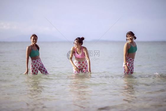 海滨蓝色的身体穿瑜伽西装的三名亚裔女站在海水中带着快乐的情绪欢笑着图片