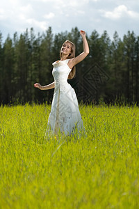 愉快白色的绿穿着婚纱年轻女孩在田里微笑和跳舞图片