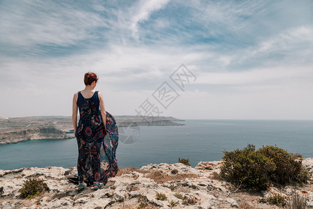 身穿长裙的红发女青年从悬崖边缘穿着长裙子随风而动户外天空自由图片