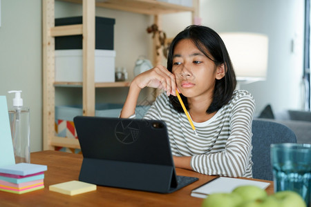 技术笔记本初级无聊的亚洲女孩在家晚上坐桌子通过互联网在线学习亚洲小生在家看电脑平板概念远程学习图片