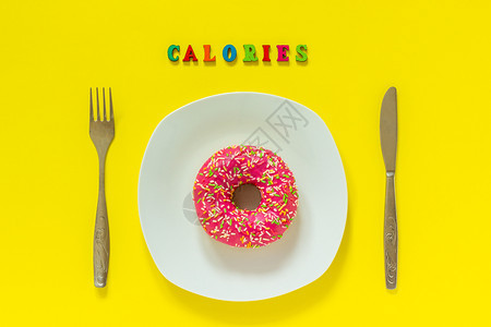 甜的小吃白板上粉红甜圈和餐具桌刀叉TextCalories仍然生活在黄色背景上红最顶端的视野平坦立体概念无饮食日卡罗乐白色盘子上图片
