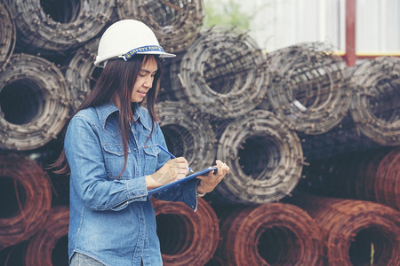 机械作坊女建筑工程师在地身戴安全白色钢帽的建筑工场薪女程师土木带有硬帽子安全头盔的女建筑工程师概念a妇女建筑工程师外部图片