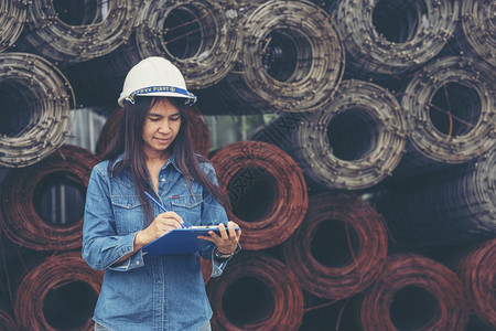 地点女建筑工程师在地身戴安全白色钢帽的建筑工场薪女程师土木带有硬帽子安全头盔的女建筑工程师概念a妇女建筑工程师设者格子图片