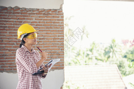 女建筑工程师在地身戴安全白色钢帽的建筑工场薪女程师土木带有硬帽子安全头盔的女建筑工程师概念a妇女建筑工程师人作蓝图图片