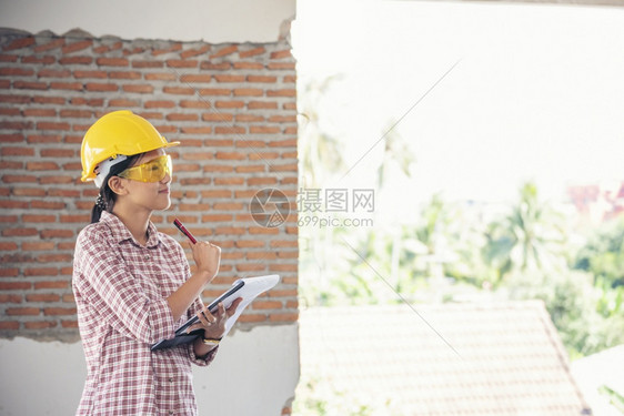 女建筑工程师在地身戴安全白色钢帽的建筑工场薪女程师土木带有硬帽子安全头盔的女建筑工程师概念a妇女建筑工程师人作蓝图图片