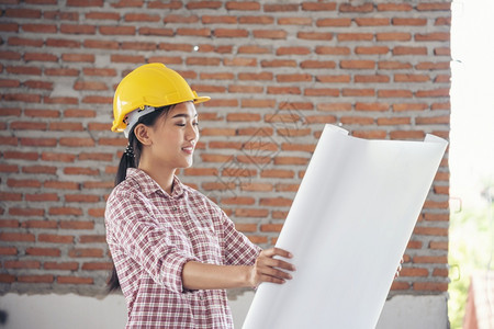 工厂穿女建筑程师在地身戴安全白色钢帽的建筑工场薪女程师土木带有硬帽子安全头盔的女建筑工程师概念a妇女建筑工程师制造业图片