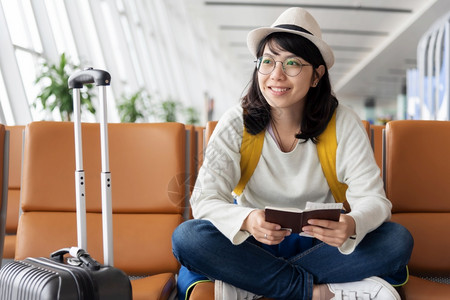 多终端坐着新鲜欢乐的亚洲女旅行者正在机场等待航班假日旅行期等手提箱背景