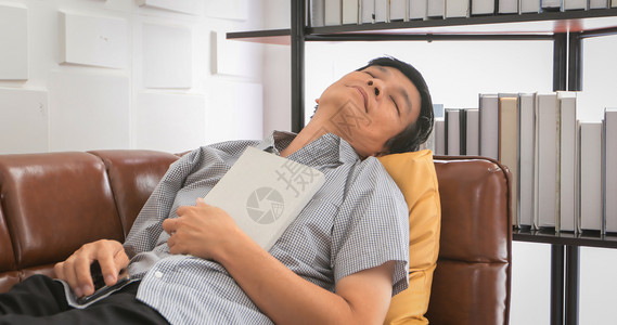 纸快乐的亚裔老人在家中客厅看书睡沙发上亚洲老年男子的肖像正在放松和幸福地阅读杂志男人图片