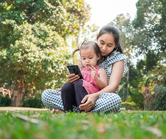 幸福父亲亚洲母和女儿坐在花园的草地上欣喜看着智能手机并坐在花园的草地上女孩图片