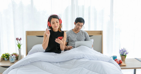 他的亚洲情侣在床上聆听音乐和歌唱并享受放松时光的快乐情绪化吉他图片