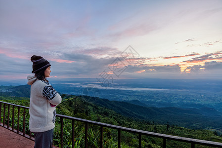地平线穿着毛衣的女游客在清晨PhuThapBoekViewpointPhetchabun高峰日出时站立观察森林和山区美丽的自然景图片