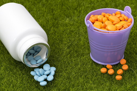 白一瓶蓝色药丸和装满橙片的桶子白一瓶蓝色药丸和填满绿草上橘片的桶子药疾病绿色图片