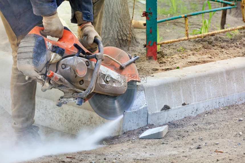 一名工人使用水泥切割机在一个建筑工地用混凝土锯切水泥截断的路面在开放的空间工人中用水泥切碎路面将段割开汽油风险具体的图片
