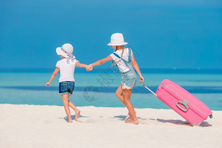 海洋可爱的小女孩带着大行李在热海滩上徒手走在热带海滩上去渡暑假小旅游女孩在热带白色海滩上拿着大手提箱的小旅行女孩子海景图片