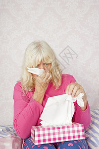 绝望吵架坏的带着粉红色睡衣和纸巾坐在床上的可怜女人吹着她的鼻子图片