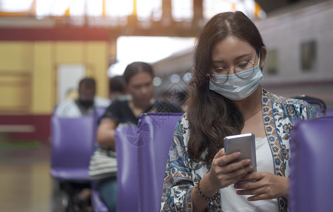 运输在休息区使用智能手机在火车站平台上等待火车的亚洲女乘客在休息区用智能手机进行保护面罩上的亚洲女乘客成人信息图片