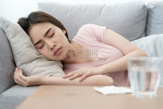 咳嗽检查温度后睡在沙发上并服用药物和水健康疾病概念亚洲女孩身体状况不健康亚洲女孩在检查温度之后睡在沙发上寒冷的图片