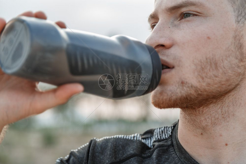 跑步一名年轻白人男子穿着黑色T恤和短裤的肖像在培训后或前从瓶子中饮用水健康积极的图片
