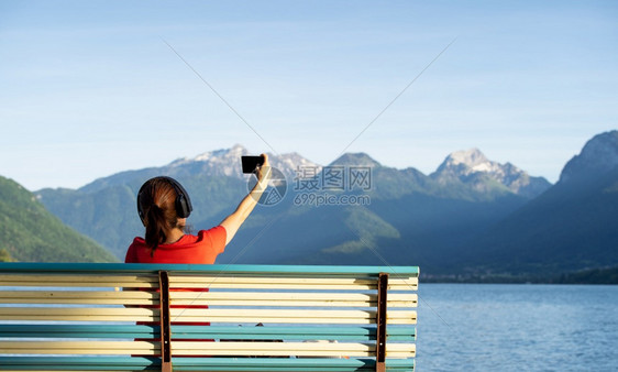 休息带着耳机的女孩坐在山前的长椅上听着湖水生活方式概念自拍闲暇景观图片