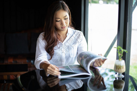 一种松弛工作亚裔女在咖啡厅微笑并阅读一本放松的书图片
