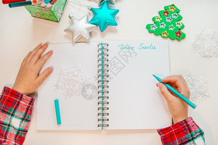 亲爱的圣诞老人信贺卡一个拿着笔的孩子在木制背景上的白纸写字带有新年装饰童梦想的礼物新年概念一个拿着笔的孩子在木头上白纸写字背景与图片