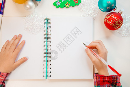 亲爱的圣诞老人信贺卡一个拿着笔的孩子在木制背景上的白纸写字带有新年装饰童梦想的礼物新年概念一个拿着笔的孩子在木头上白纸写字背景与图片