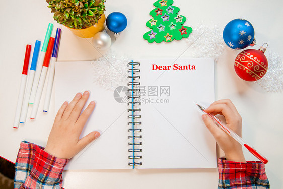 快乐的问候亲爱圣诞老人信贺卡一个拿着笔的孩子在木制背景上的白纸写字带有新年装饰童梦想的礼物新年概念亲爱的圣诞老人信贺卡一个拿着笔图片