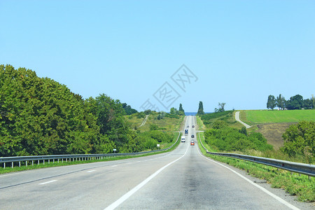 高速公路很远沥青两边有树木和灌蓝色的路边图片