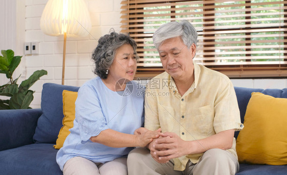 女士辅助年长的亚裔高龄女在家中客厅沙发上坐在时安抚其丈夫使免于情绪压抑老旧的退休生活方式妻子图片