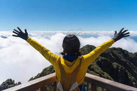 制作者穿着黄色毛衣的亚洲快乐女旅行者正站在山上云中和天空高举双臂在度假后视线上站立享受新鲜图片
