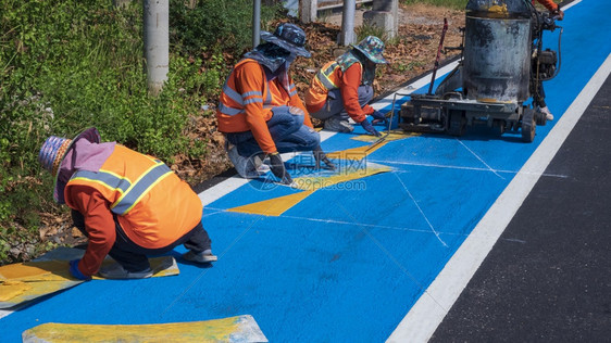 工人带有热塑料喷雾路标识仪的反射背心路工组正在对沥青路面的交通线和自行车道进油漆有选择地聚焦点盘子在职的图片