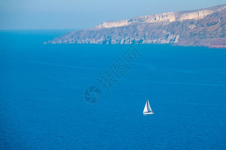 希腊圣托里尼多岩石的在阳光明媚日落白帆游艇空中观光白帆游船荡在落雪海岸附近太阳尼日白色的圣托里尼背景