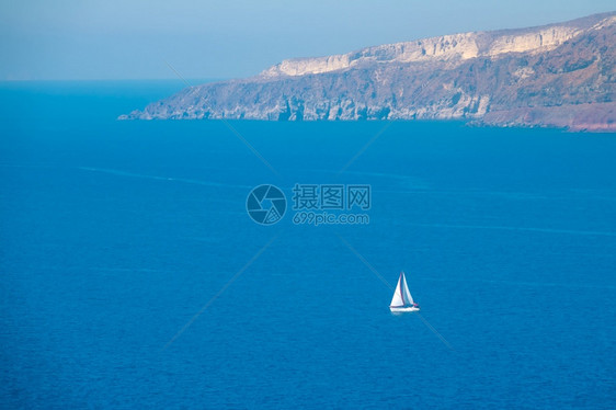 多岩石的在阳光明媚日落白帆游艇空中观光白帆游船荡在落雪海岸附近太阳尼日白色的圣托里尼图片