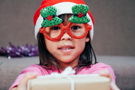 倾斜圣诞老人快乐的小女孩戴着圣诞帽在家送礼物新年快乐圣诞前夕图片