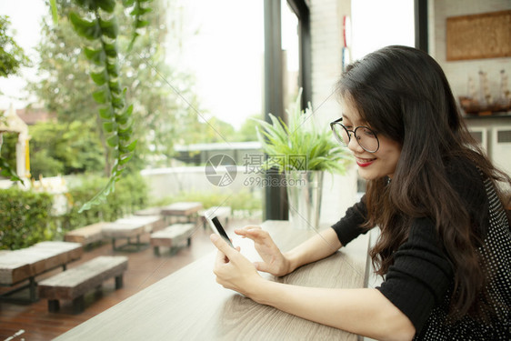 屋单身的美丽亚洲年轻女带着快乐的情绪笑阅读智能手机泰国图片