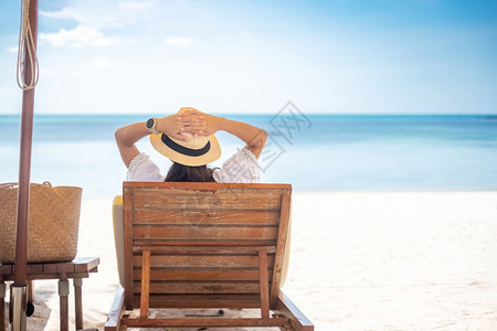 岛穿着白色衣服和帽子的快乐旅行妇女享有美丽的海景年轻女坐在椅子上热带海滩看洋自由放松假期和暑旅行概念享受着美丽的海景快乐年轻背景