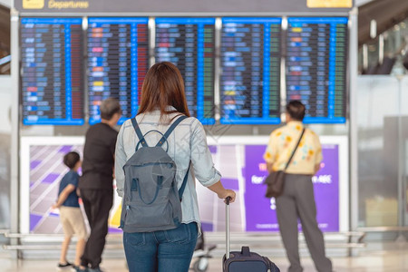 在现代机场旅行和运输概念的飞行信息屏幕上登入机检查时背着行李站在飞板上的亚洲女旅行者背面在飞信息屏幕上登机国际的游客木板图片