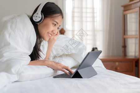 人们微笑声音的美丽亚洲年轻女肖像正在休息床上监听音乐用平板电脑在家中娱乐用听音机与亚洲女孩一起睡觉图片