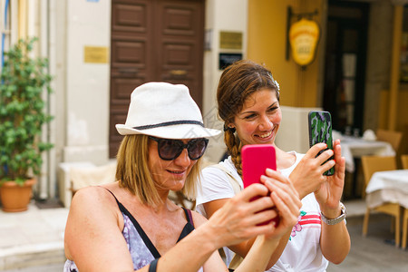 看乐趣2名美丽的旅游女客在夏天使用手机拍摄自照片在老城街的旧道上拍照漂亮的图片