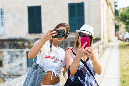 2名美丽的旅游女客在夏天使用手机拍摄自照片在老城街的旧道上拍照女技术友谊图片