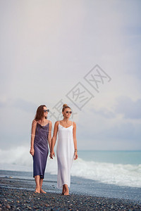 健康天堂泻湖海滩上年轻美丽的女孩一起散步在海滩上穿白衣服的年轻女人图片