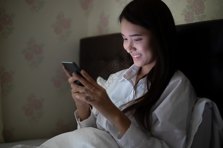 屋震惊晚上在床使用手机的亚洲妇女她笑着在家里享受快乐卧室图片
