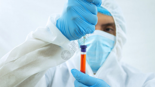 保持脸技术身着生物防护服面罩和蓝色手套的拉丁医生在白色背景上用注射器在试管中抽取血液样本的特写视图身着生物防护服面罩和蓝色手套的图片
