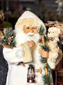 穿着白色皮毛大衣的圣诞老人装饰玩具白皮大衣上挂着鲜树枝锥子手头上的一根旧灯和只小泰迪熊快乐的传统他图片
