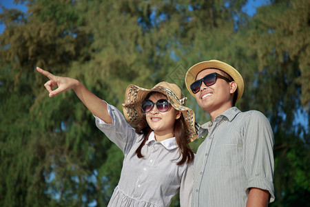 肖像幸福约会夏天亚洲夫妇在海滩指着他们的手穿着太阳眼镜的男人和女笑着看海大的面容图片