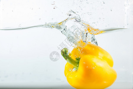 健康清除甜辣椒在水中喷洒黄色的白背景甜辣椒是一种不新鲜的图片