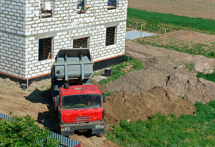 加里宁格勒结石卡车和房子的是用白砖建造的自卸车把沙子带到建筑物上自卸车靠近正在建造的房子翻斗车靠近正在建造的房子卡车和是用白砖建背景图片