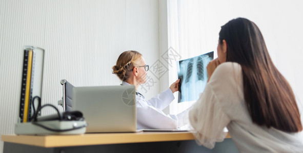 扫描考试白种人老年女医生在院诊断病室的疗内持有和看年轻女病人X光片有关CoronaLungCovid19的诊断疾病图片